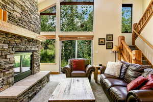 Carpeted living room featuring a high ceiling, stairs, and a stone fireplace