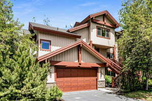 View of front of home with asphalt driveway, a garage, stairs, and roof with shingles