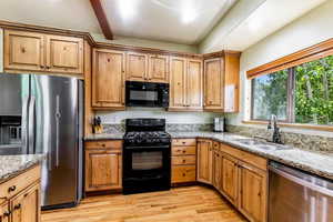 Kitchen featuring black appliances, light wood-style flooring, light stone counters, and beam ceiling