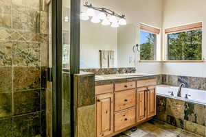 Full bath featuring double vanity, a garden tub, and stone finish floors