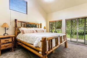 Carpeted bedroom with high vaulted ceiling and access to exterior