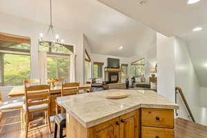 Kitchen with vaulted ceiling, dark wood-style floors, light countertops, a center island, and a glass covered fireplace