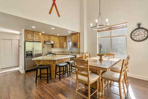 Dining space with a chandelier, plenty of natural light, a high ceiling, dark wood-style floors, and recessed lighting