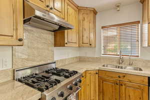 Kitchen featuring stove, under cabinet range hood, light countertops, and decorative backsplash