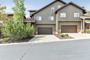 View of front facade with roof with shingles, stone siding, an attached garage, and driveway