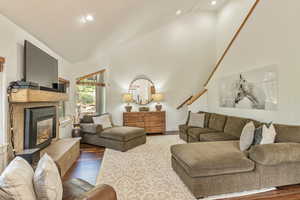 Living area with wood finished floors, a glass covered fireplace, vaulted ceiling, recessed lighting, and stairs