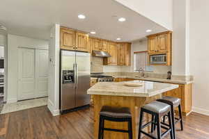 Kitchen featuring appliances with stainless steel finishes, under cabinet range hood, light countertops, dark wood-type flooring, and a kitchen island