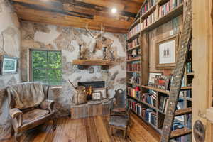 Living area with hardwood / wood-style flooring, a stone fireplace, and a wooden ceiling with exposed beams