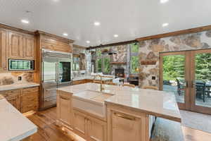 Kitchen with built in appliances, a fireplace, french doors, light wood finished floors, and light stone countertops