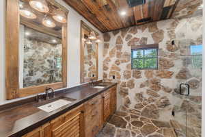 Full bathroom featuring wood ceiling, double vanity, and a shower stall