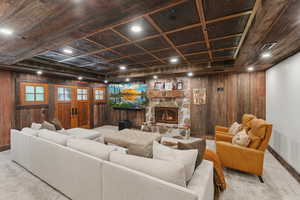 Carpeted living area with wooden walls, french doors, and a stone fireplace