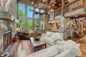 Living room featuring hardwood / wood-style flooring, a towering ceiling, a fireplace, beamed ceiling, and a chandelier