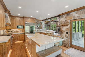 Kitchen with built in appliances, premium range hood, light wood-type flooring, a kitchen breakfast bar, and a stone fireplace