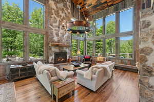 Living area featuring high vaulted ceiling, wooden ceiling, hardwood / wood-style floors, a chandelier, and a stone fireplace