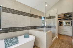 Full bathroom featuring a shower stall, wood finished floors, a soaking tub, a walk in closet, and lofted ceiling