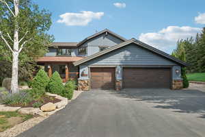 View of front facade featuring driveway, stone siding, and an attached garage