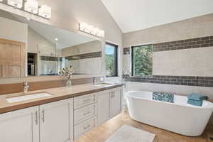 Full bath with vaulted ceiling, double vanity, a shower stall, a freestanding tub, and wood finished floors