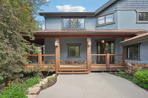 Doorway to property featuring covered porch, stone siding, and stucco siding