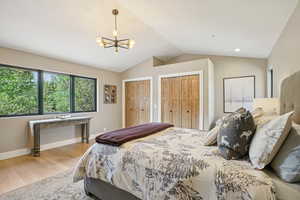 Bedroom featuring two closets, vaulted ceiling, a chandelier, and wood finished floors