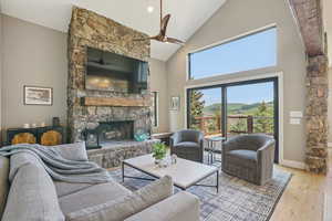 Living room with a ceiling fan, a stone fireplace, high vaulted ceiling, and wood finished floors