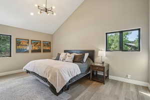 Bedroom with high vaulted ceiling, multiple windows, a chandelier, and wood finished floors