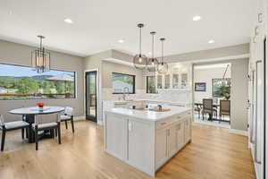 Kitchen featuring a chandelier, light countertops, backsplash, glass insert cabinets, and white cabinetry