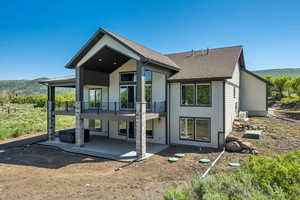 Rear view of house with a patio, a balcony, and a shingled roof