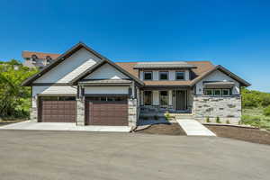 View of front facade featuring stone siding, a garage, covered porch, and roof with shingles