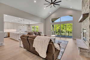 Living area with recessed lighting, a fireplace, a ceiling fan, high vaulted ceiling, and light wood-style flooring
