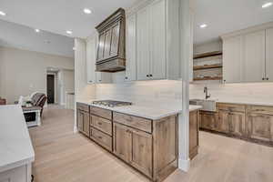 Kitchen featuring stainless steel gas stovetop, light wood-style floors, open shelves, tasteful backsplash, and recessed lighting