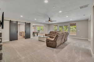 Living room with a barn door, billiards table, a ceiling fan, light colored carpet, and recessed lighting