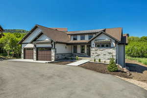 View of front facade featuring a standing seam roof, stone siding, a metal roof, and a garage