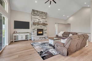 Living room featuring high vaulted ceiling, ceiling fan, light wood-style floors, a fireplace, and recessed lighting