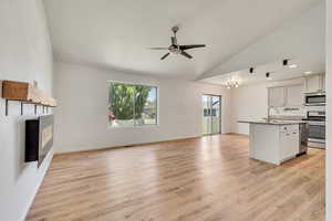 Unfurnished living room with a ceiling fan, lofted ceiling, light wood-style flooring, and a glass covered fireplace