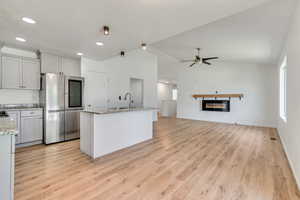 Kitchen with smart refrigerator, light wood finished floors, lofted ceiling, ceiling fan, and a glass covered fireplace