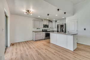 Kitchen featuring appliances with stainless steel finishes, light wood finished floors, light stone countertops, a kitchen island with sink, and recessed lighting