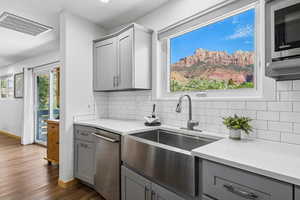 Kitchen with gray cabinetry, stainless steel dishwasher, dark wood-type flooring, and tasteful backsplash