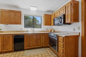 Kitchen with black appliances, light flooring, brown cabinets, and light countertops