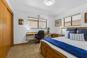 Bedroom with light carpet, baseboard heating, a desk, and a closet