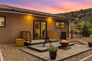 Back of property at dusk featuring an outdoor fire pit, a patio area, stucco siding, and a mountain view