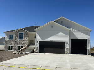 View of front facade featuring stone siding, board and batten siding, driveway, and a garage