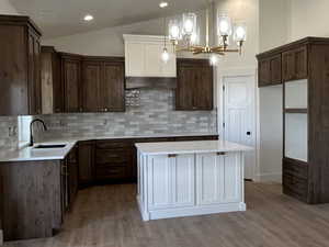 Kitchen featuring hanging light fixtures, vaulted ceiling, tasteful backsplash, a kitchen island, and wood finished floors