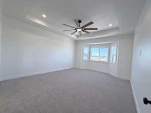 Spare room with a tray ceiling, light carpet, ceiling fan, and recessed lighting