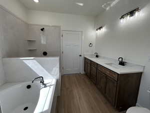 Bathroom featuring a garden tub, double vanity, light wood-type flooring, and tiled shower