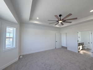 Unfurnished bedroom with a tray ceiling, carpet flooring, recessed lighting, ceiling fan, and ensuite bathroom