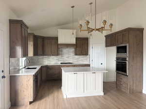 Kitchen with lofted ceiling, white cabinets, appliances with stainless steel finishes, a center island, and pendant lighting