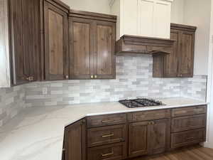 Kitchen featuring tasteful backsplash, light stone counters, dark brown cabinetry, and custom exhaust hood
