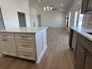 Kitchen featuring light stone countertops, light wood finished floors, lofted ceiling, pendant lighting, and a chandelier