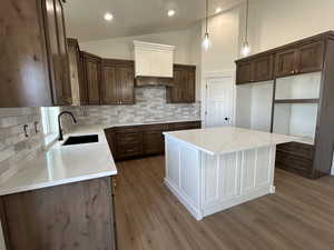 Kitchen featuring backsplash, a center island, light stone countertops, vaulted ceiling, and decorative light fixtures