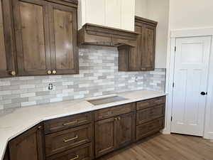 Kitchen with backsplash, light wood-style floors, light stone countertops, and black electric cooktop